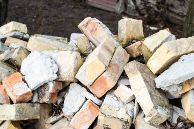 Arsanın yanındaki eski duvarda çizikler ve çatlaklar olan bir yığın kullanılmış tuğla..