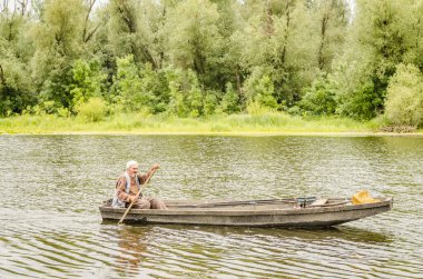 A sport fisherman rides on a pond in a wooden boat with the help of an oar.
