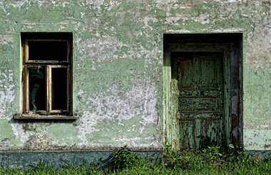 An old wooden door and a broken window with a dilapidated antique decorative white wooden frame, placed on the wall of the family house.
