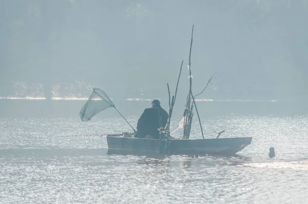 一个渔夫在湖面上的一条木船上 周围是晨雾和秋日的余晖 — 图库照片
