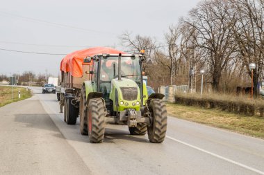 Novi Sad, Sırbistan - Mart 05. 2021: Karavanı olan yeşil bir tarım traktörü karayolunda sürüyor.