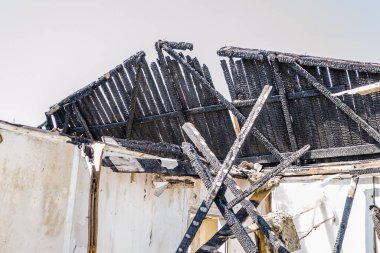 The remains of the burnt house. Ruined and collapsed house burnt and damaged in the fire with remains of the wooden reinforcement poles of roof selective focus. Burned house