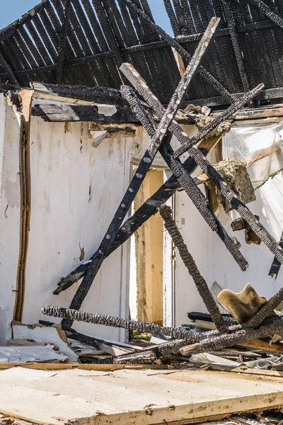 The remains of the burnt house. Ruined and collapsed house burnt and damaged in the fire with remains of the wooden reinforcement poles of roof selective focus. Burned house