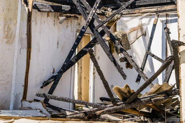 The remains of the burnt house. Ruined and collapsed house burnt and damaged in the fire with remains of the wooden reinforcement poles of roof selective focus. Burned house