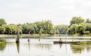 Sports fisherman in a wooden boat. A sports fisherman sits in a wooden boat on the water in the summer, lit by the sun.