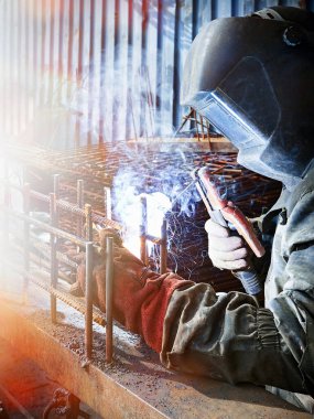 A welder works at a construction fittings manufacturing site. Industrial background.