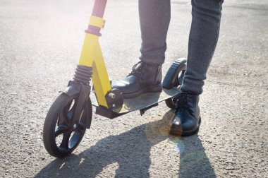 Scooter 'a binmek üzere olan bir çocuğun yakın çekimi. Motosikletli kızın bacakları yolda.
