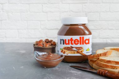 KREMENCHUG, UKRAINE - 9 Ekim 2021: Nutella cam kavanozu mutfakta kahvaltıda taze pişmiş ekmek. Tatlandırılmış fındıklı kakao. İtalyan şirketi Ferrero 'nun çok popüler markası.