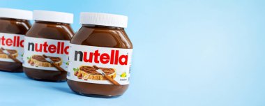 KREMENCHUG, UKRAINE - 9 Ekim 2021: fındıklı kakao ezmesi. Üç cam kavanoz çikolatalı fındık sancağının afişi mavi arka planda fotokopi alanı ile yayılmış.