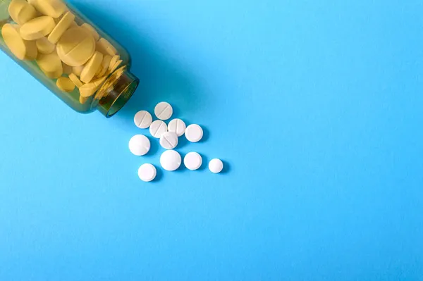 白色圆形药丸分散在蓝色背景的棕色瓶子上 药学和保健主题 医疗背景 复制空间 成瘾治疗 社会健康问题概念 — 图库照片