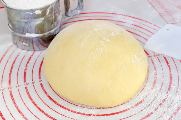 Raw yeast dough on the floured silicone baking mat with markings on the kitchen table.