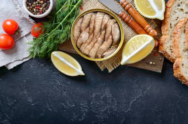 Açık teneke kutuda füme sardalya, çıtır tahıl ekmeği, yeşillik, limon, taze domates. Üst manzara, düz yatış. Kopyalama alanı olan yiyecek arkaplanı.