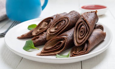 Beyaz ahşap bir masada beyaz bir tabakta yuvarlanmış çikolatalı krep. Bir yığın çikolatalı krep. Seçici odak.