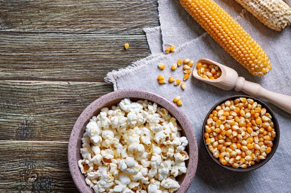 Corn kernels, cob, freshly popped popcorn on wooden background with copy space. Cooking popcorn.