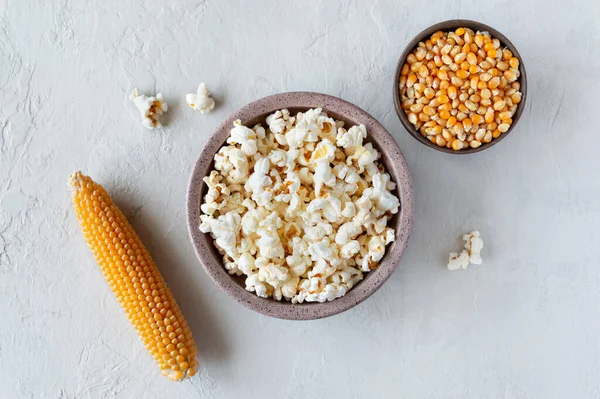 Prepared popcorn in bowl, corn seeds and corncobs on concrete background. The top view