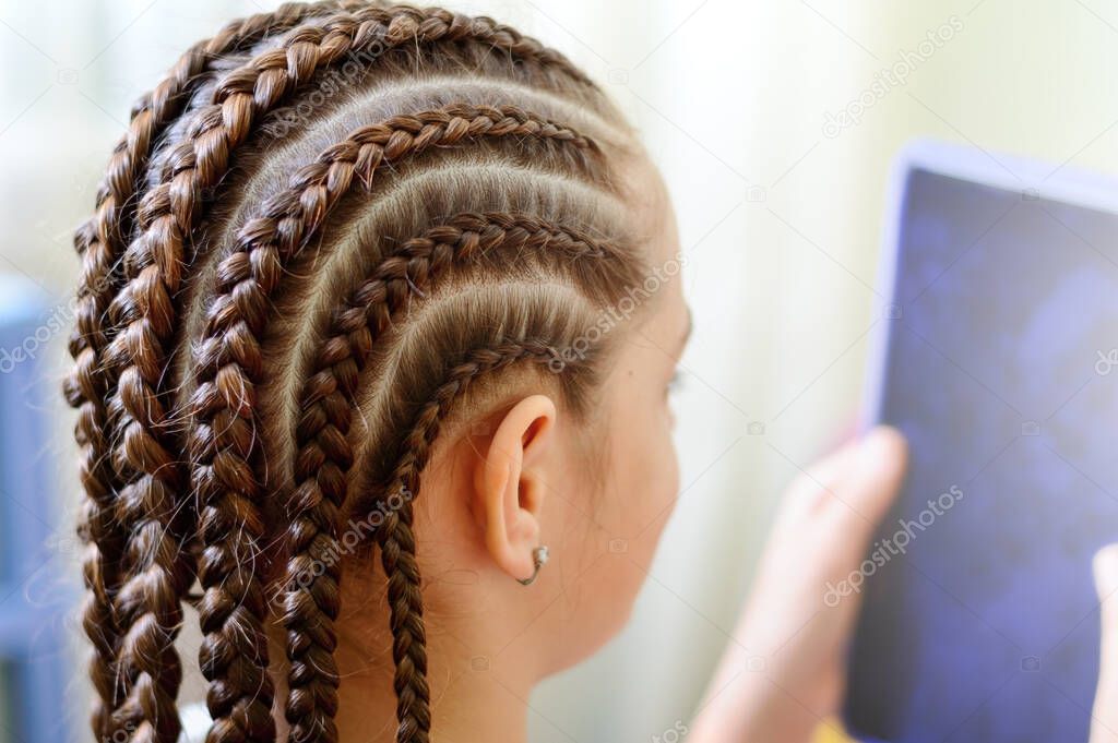 Girl with many small braids holding the tablet in front of him. Close-up, selective focus