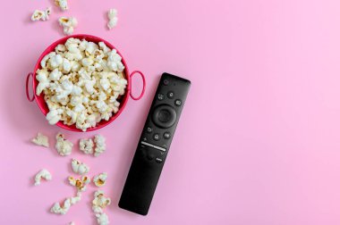Metal kasede patlamış mısır ve kopyalanmış pembe arka planda uzaktan kumanda. Boş zaman, film, şov, spor konsepti.