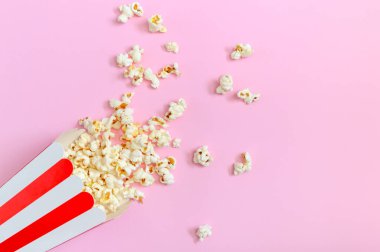 Patlamış mısır, çizgili bir kağıt bardaktan kopyalanmış pembe bir zemin üzerine dökülmüş. Boş zaman, film, şov, spor konsepti.