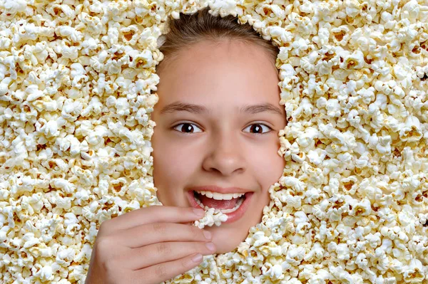 Young beautiful girl face smiles in popcorn has delicious snack. Head through air popped corn. People and entertainment concept.