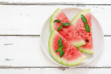 Slices of fresh fresh watermelon on a plate on a white wooden background. Fruit and mint to quench thirst. Top view with copy space.