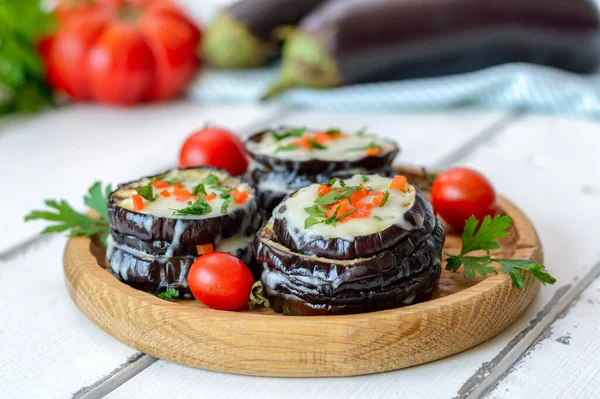Eggplant baked with mozzarella cheese, tomatoes on a wooden plate.  Vegetarian food recipe.