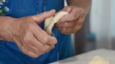 Kırışık ellerin yakın çekimi hamuru yoğurur ve ev yapımı çörekler hazırlar. Masanın üstünde büyükannenin elleri ve çiğ hamuru var. Aşçılık gelenekleri, aile tarifleri..