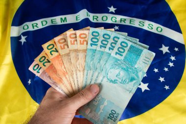 Elinde Brezilya para banknotları, arkasında Brezilya bayrağı var..