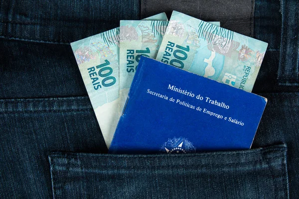 Brazilian document work and social security (Carteira de Trabalho e Previdencia Social) in the pocket of his jeans with one hundred reais bills. brazilian money.