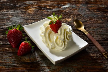 Kırsal bir masada beyaz bir fincan tabağında servis edilen kremalı lezzetli çilekler. 