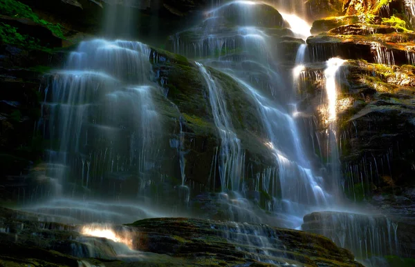 Moving water cascade of a creek with light reflections and black and colored rocks.