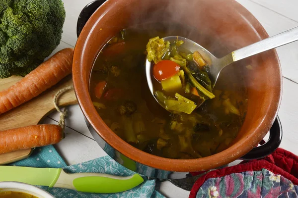 Hot vegetable soup in an earthenware pan with a ladle of steaming soup