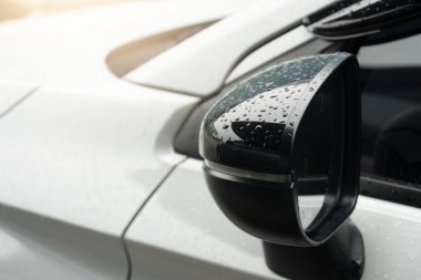 Kapalı ayna kanat siyah beyaz araba rengi. Ayna kanadında yağmur damlası var. Ön camın kenarından parlak bir ışık geldi..