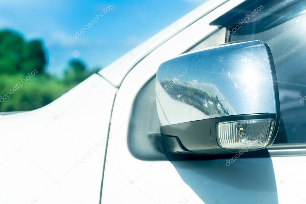 Close up side mirror wing of car  is foldable parking time. parking outdoor at day time. with blurred of trees under blue sky.