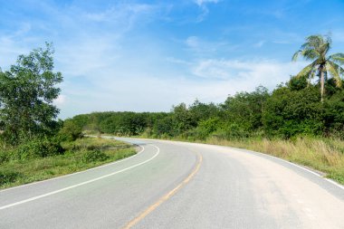 Asfalt yolu boyunca uzanan kıvrımlı patikada Tayland 'da yolun tepesinde kum var. Yeşil çimenlerin ve ağaçların yanında. Mavi gökyüzünün altında.