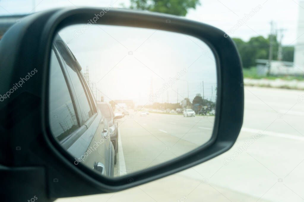 Abstract and blurred view of traffic from behind through the mirrors wing of a gray car. with abstract of shining from behind.