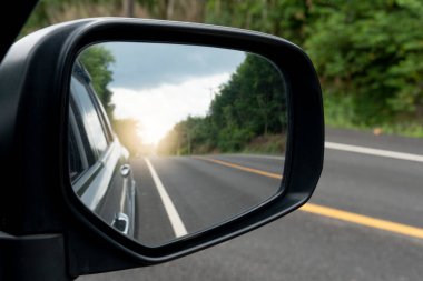 Ayna kanadının iç görüntüsü. Gündüz vakti asfalt yolu ve yeşil ağaçları olan gri bir arabanın arka manzarası. Kırsal bölgelerdeki trafiği temizle.