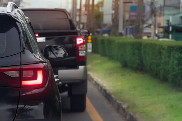 Rear side of black car on the asphalt road heading towards the goal of the trip. Traveling for work during rush hour. Environment of blurred of other cars in the city. Island of green grass beside.