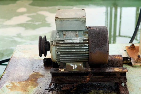 Used of pressure pump mounted on a rusted steel base rests on a damp plaster floor. Machine operation in industrial processes.