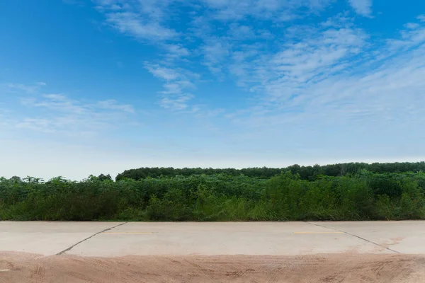 Tayland 'daki beton yolun yatay görüntüsü. Toprak yolların ve yüzen lastiklerin önünde. Yeşil çimenlerin arka planı. Cassava tarlaları ve kauçuk ağaçlarının genç tohumları. Mavi gökyüzünün altında.