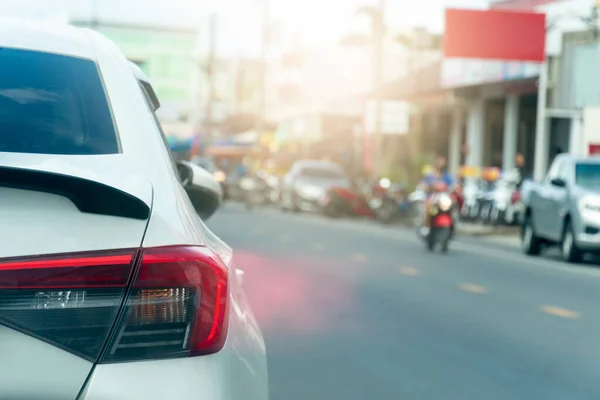 Rear of the car and taillight of white car on the asphalt road. with turn brake light. blurred environment of city other cars and motorcycle.