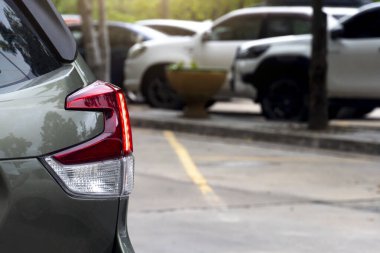 Rear side of car with turn on tail light in parking lot. Blurred of several cars were parked facing into the car park under the shade of the trees. on concrete road.