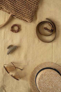 Sarı muslin kumaşlı kadın plaj aksesuarları. Kemer, hasır çanta, güneş gözlüğü, şapka, güneş gözlüğü. Seyahat blogu için estetik bohem konsepti, sosyal medya. Düz yatış, üst görünüm