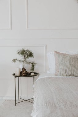 Yatak odası komodinli, yataklı nötr çarşaflı, yastıklı, beyaz duvarlı. Noel için tasarlanmış modern minimalist ev dekorasyonu