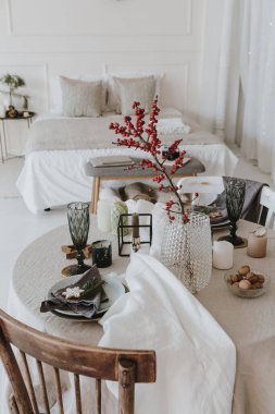 Zarif bohem iç tasarımı. Ahşap sandalyeli yemek odası, süslemeli masa, bej kumaş, kırmızı dut buketi, mumlar. Modern daire, ev dekorasyonu..