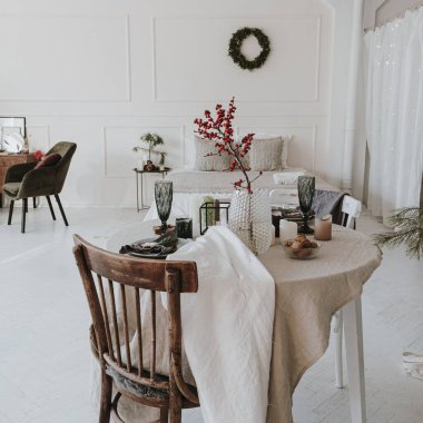 Zarif estetik Noel yemeği servis konsepti. Parlak oturma odası sandalyeli, bej masa örtülü masa, böğürtlen buketi. Noel kutlaması akşamı