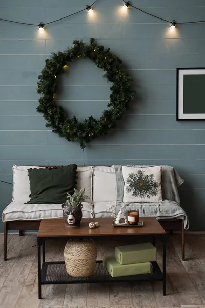 現代のホームインテリアデザインコンセプト クリスマスリースフレーム ソファ テーブル ギフトボックス ガーランドライトで飾られた快適な居心地の良いリビングルーム クリスマスお正月のお祝いの飾り — ストック写真