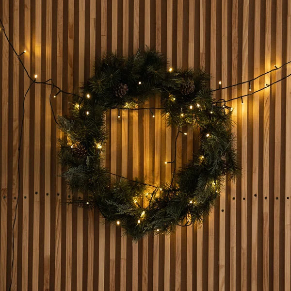 Aesthetic Scandinavian hygge home interior: warm glowing garland lights, Christmas wreath hanging on wooden rails wall. Christmas, New Year holidays decor