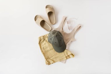 Beyaz arka planda yaz soğuğu için kadın kıyafetleri olan en düşük moda konsepti. Bej ayakkabılar, üst, güneş gözlüğü, şort, şapka. Düz yatış, üst görünüm