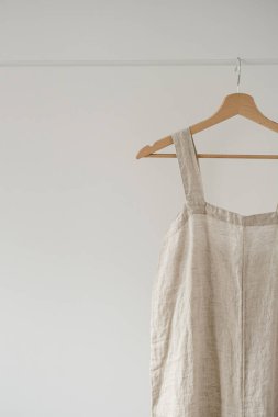 Minimalist gardırop: nötr bej renkli tulum ya da beyaz duvara asılı elbise. Estetik moda konsepti