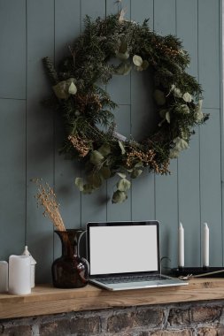 Önde dizüstü bilgisayarın boş fotokopi ekranı, rafta mumlar, çiçek buketi var. Tozlu mavi duvarda Noel çelengi asılı. Sosyal medya, blog, web sitesi markalaşma şablonu